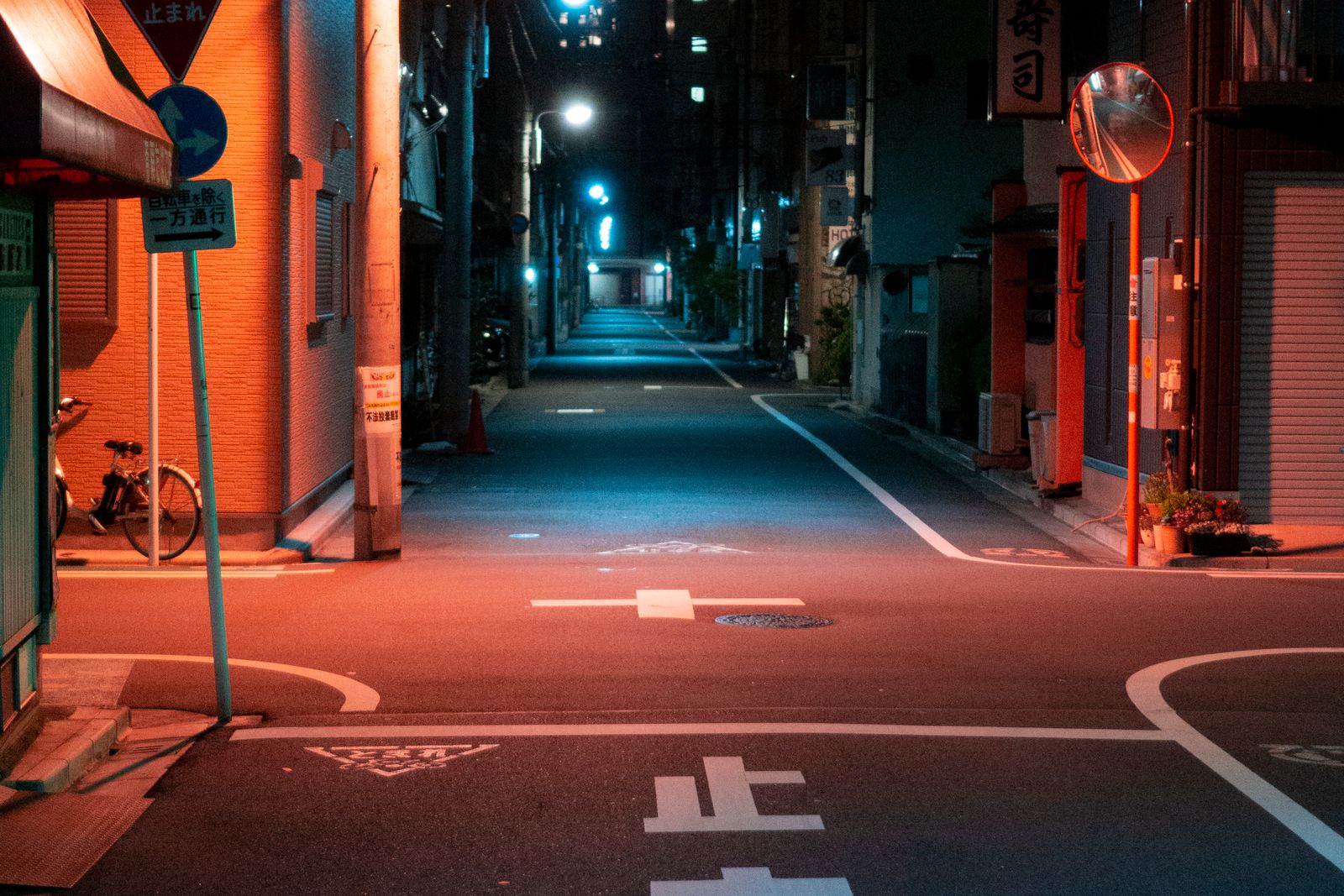 An empty, well-lit residential back street at night with 止まれ painted on the road surface.