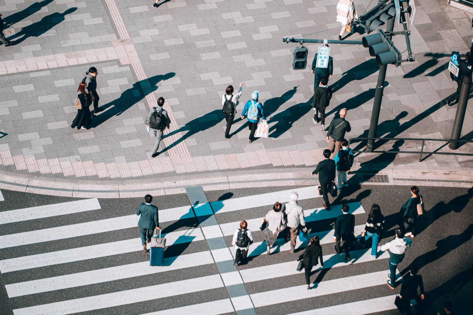 An ordinary Japanese street crossing photographed from above in flat daylight, around thirty people walking across it.