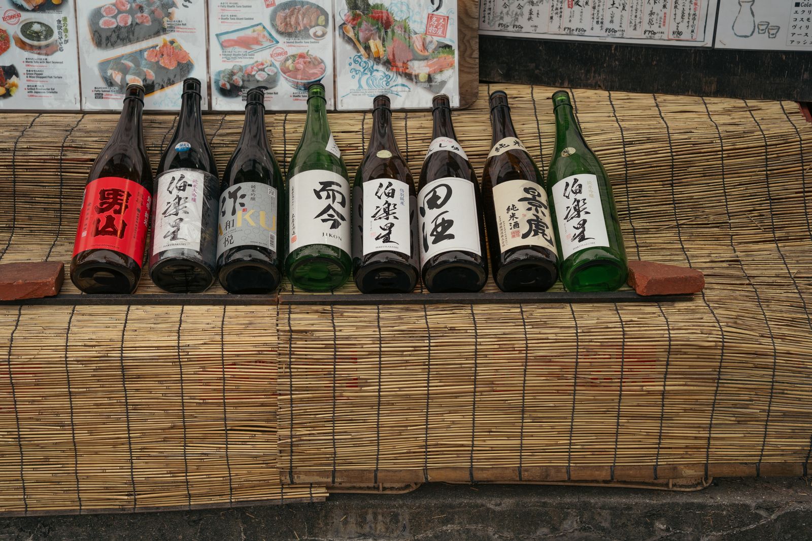 Eight large sake bottles displayed under a hand-set drinks board.