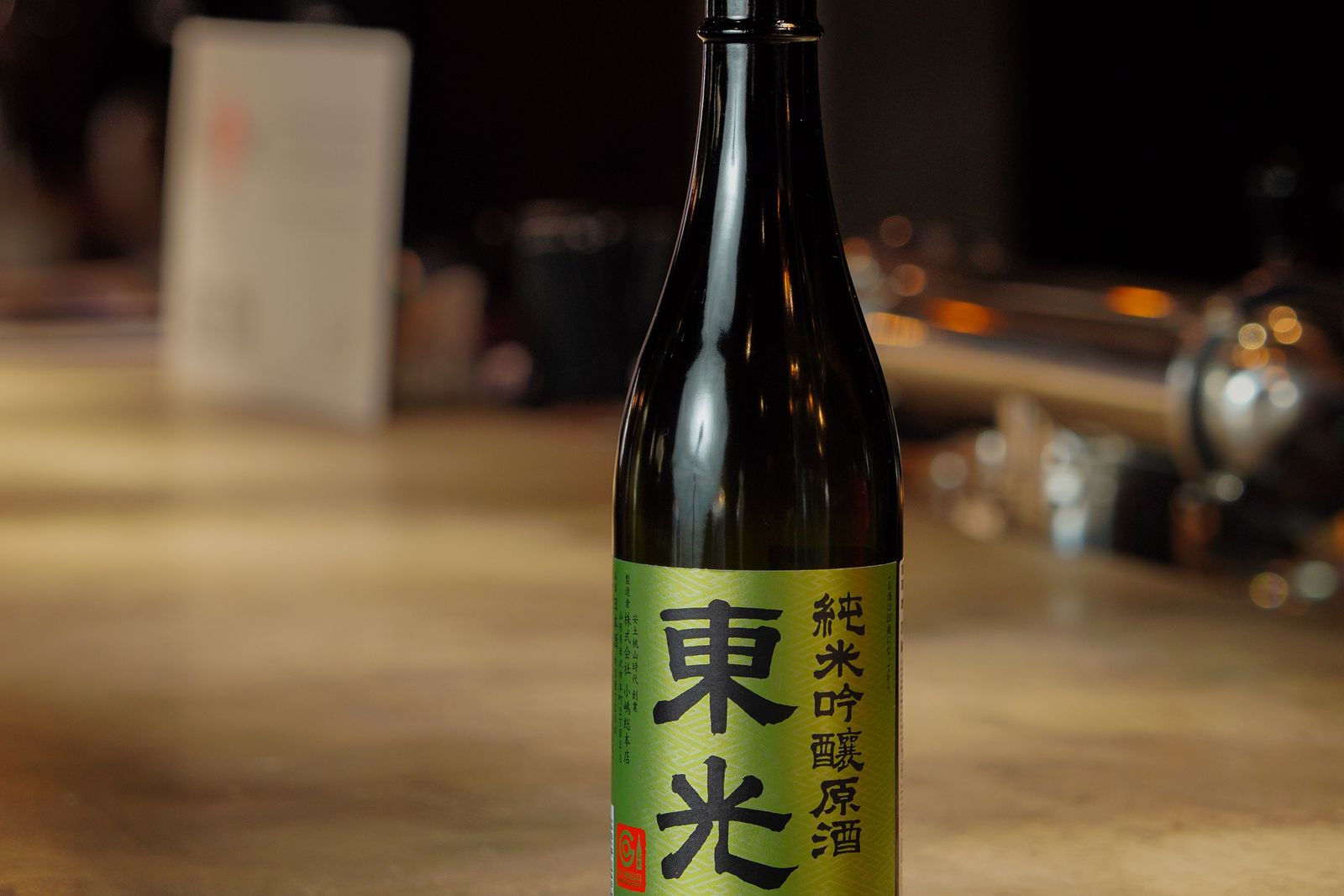 A dark sake bottle on a wooden counter, its front label legible.