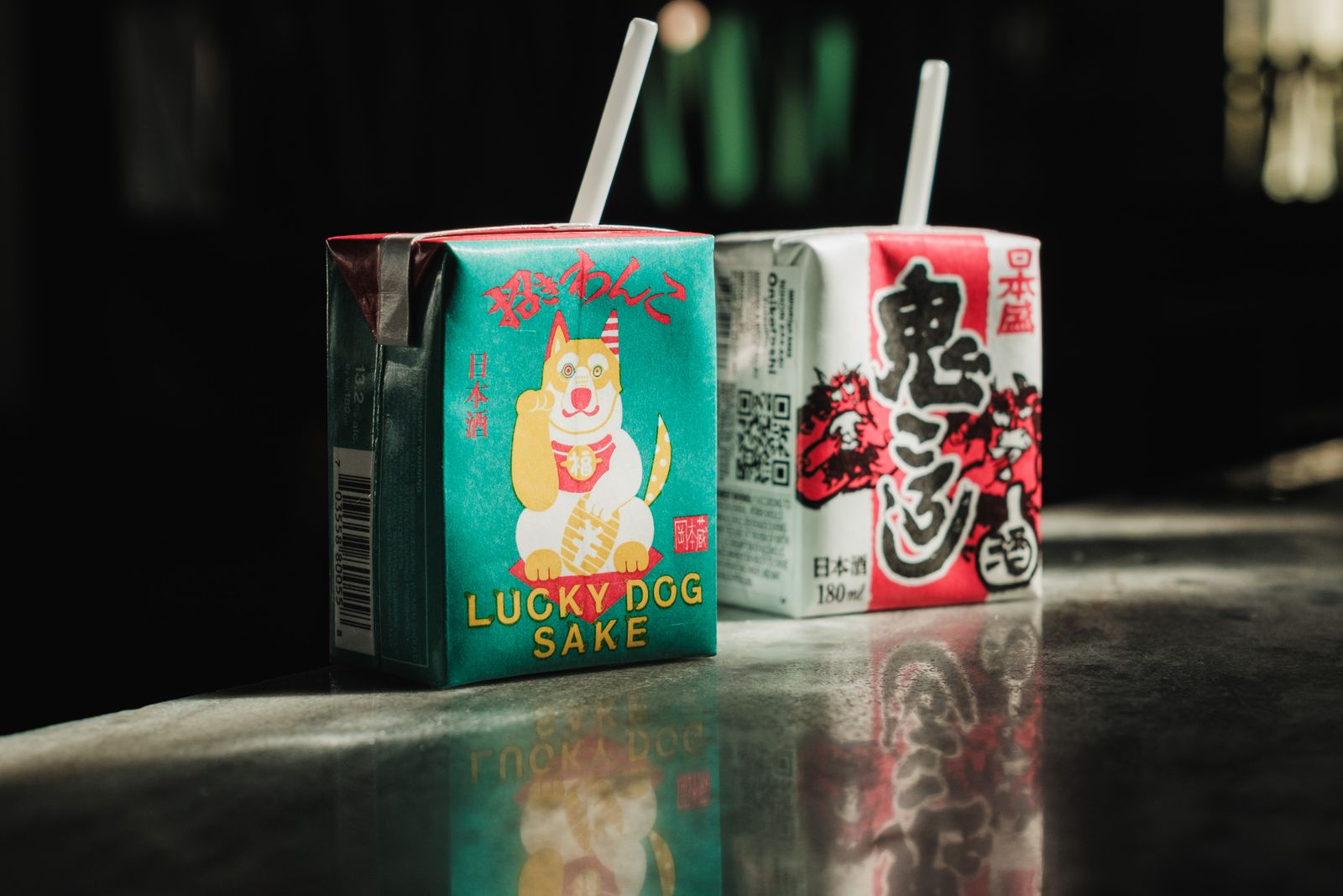 Two small paper cartons of Japanese sake with straws attached.