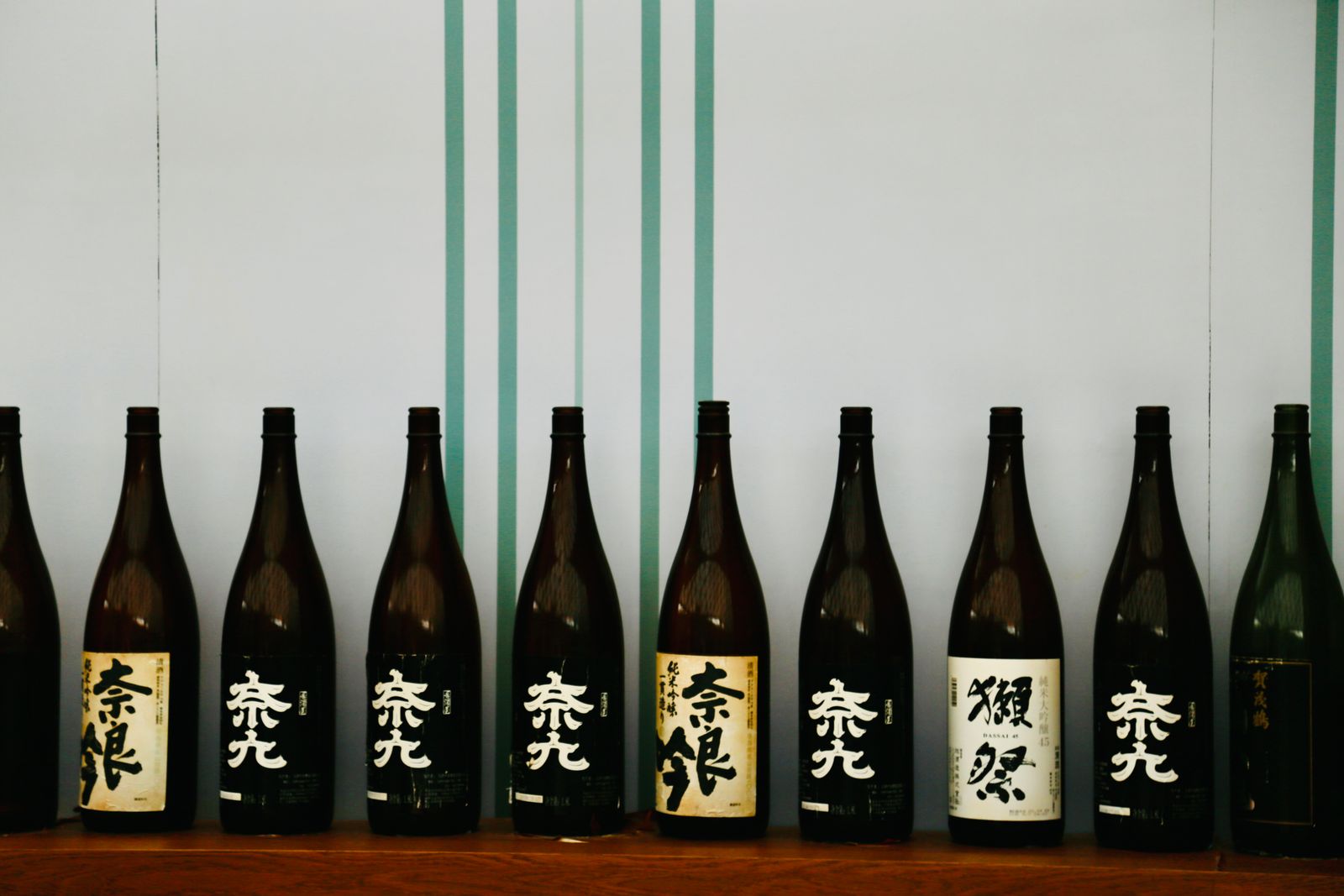 Ten large sake bottles standing in a row on a wooden shelf.