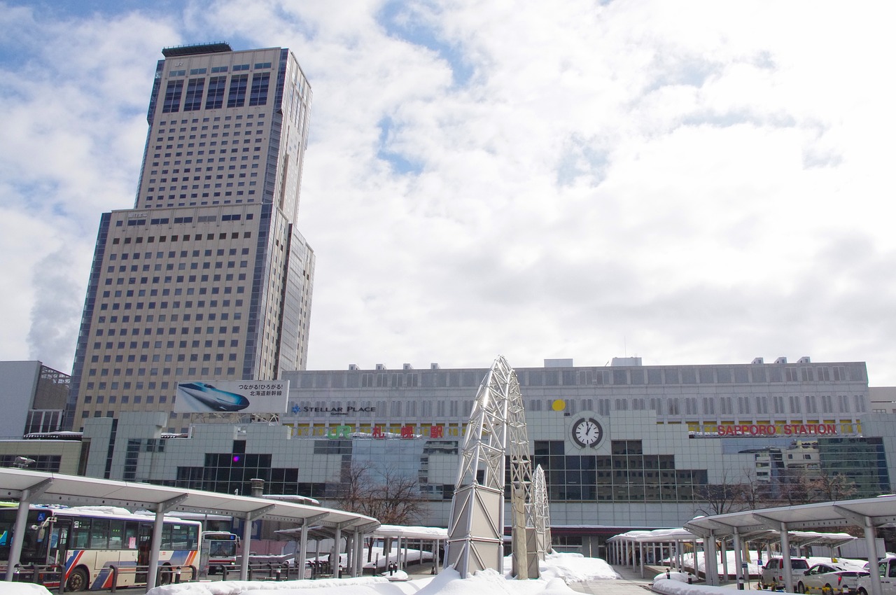 The north side of JR Sapporo Station in winter, the JR Tower high-rise on the left, snow banks and bus-stop canopies in front.