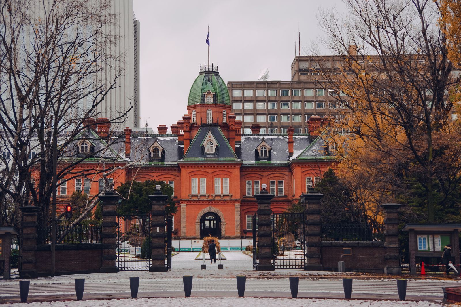 The red-brick Former Hokkaido Government Office Building with its green dome, seen through the front gates in late autumn with early snow