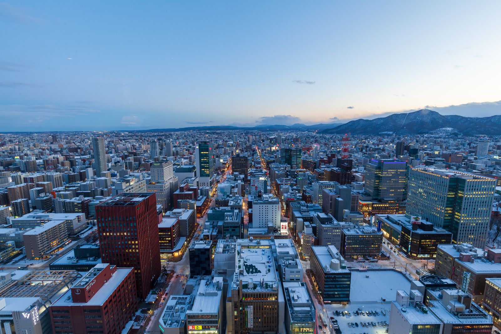 Central Sapporo from above at winter dusk, snow on the rooftops and low mountains on the horizon