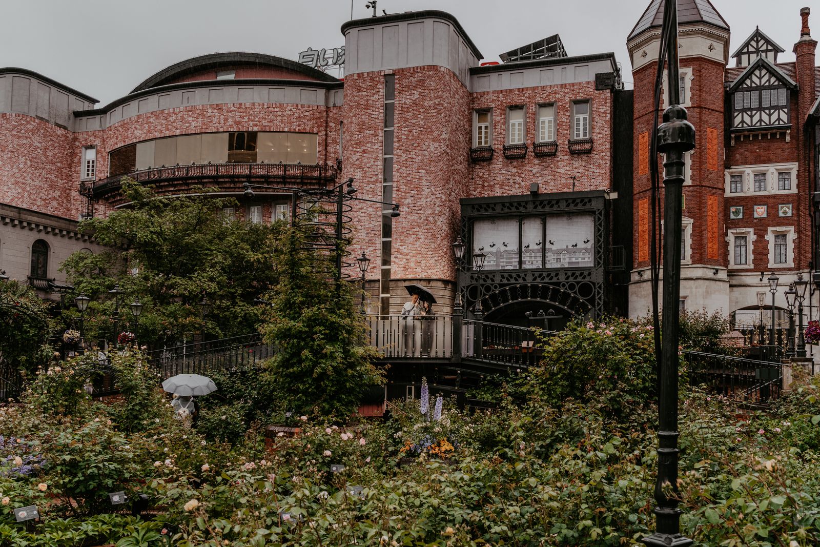 The brick buildings of Shiroi Koibito Park behind its garden on a rainy day