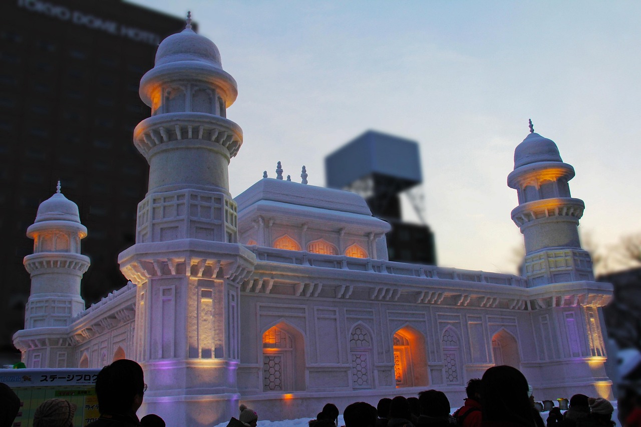 A large snow sculpture lit at dusk during the Sapporo Snow Festival, visitors in the foreground