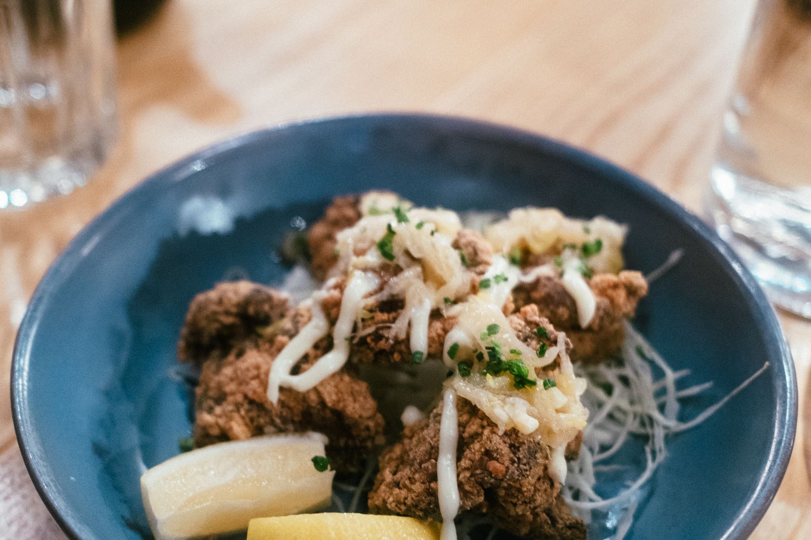 Pieces of Japanese-style fried chicken with mayonnaise and lemon wedges on a blue plate.
