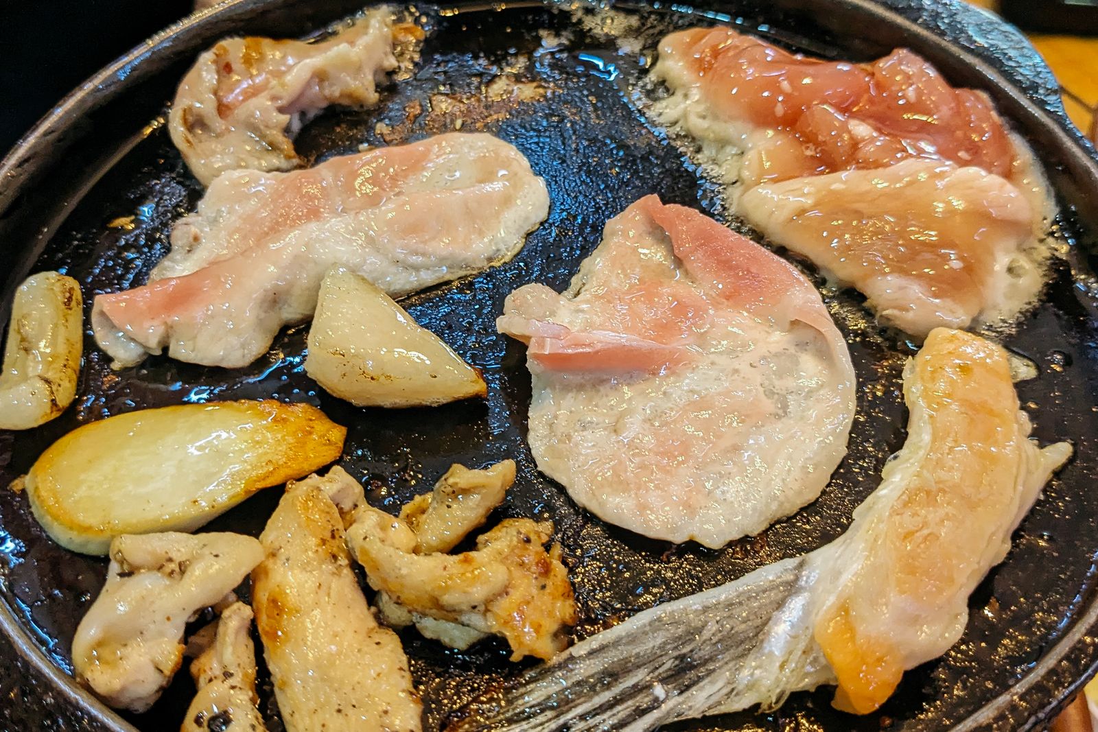 Thin slices of meat and onion cooking on a rounded cast-iron grill pan over a tabletop burner.