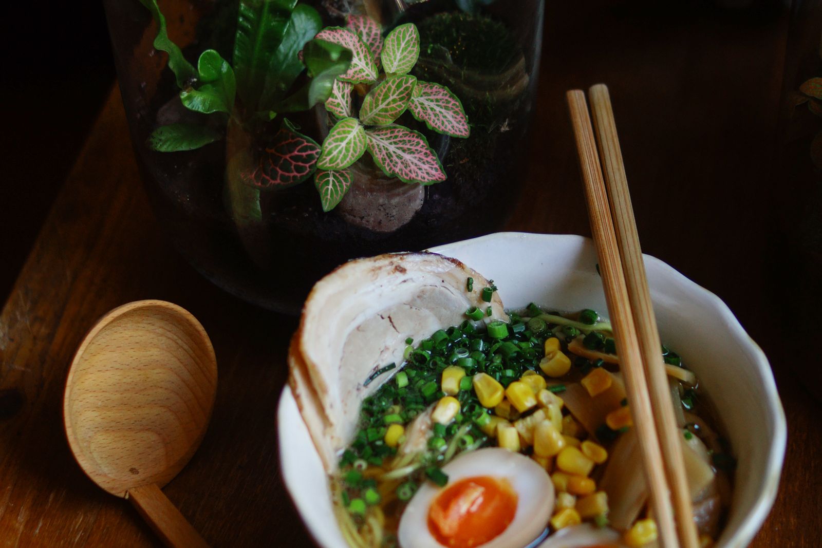 A bowl of ramen topped with corn, scallions, a slice of chashu and two half soft-boiled eggs, with chopsticks resting on the rim.