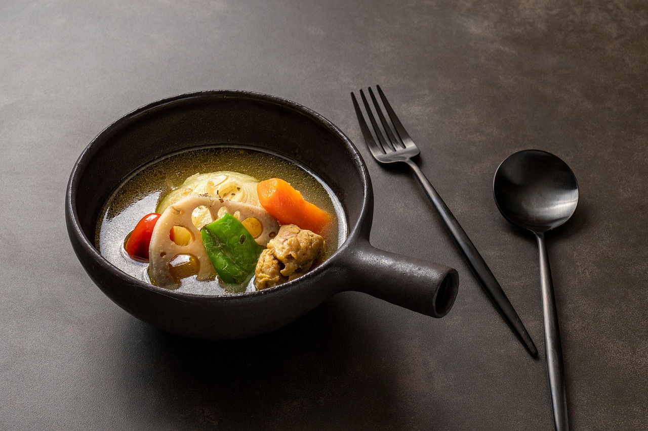 A bowl of thin curry-spiced soup with lotus root, carrot, cabbage, a green pepper, a tomato and a piece of chicken.
