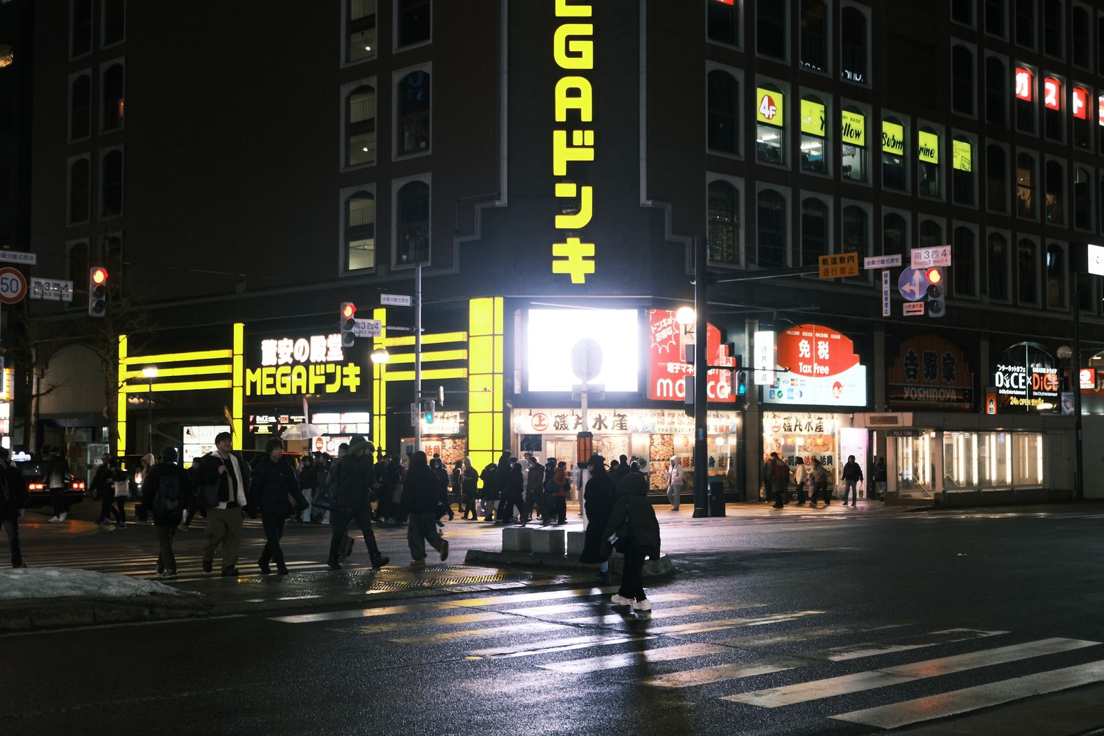 A busy night crossing at South 3 West 4 in Sapporo, pedestrians on the zebra crossing under bright storefront signs.