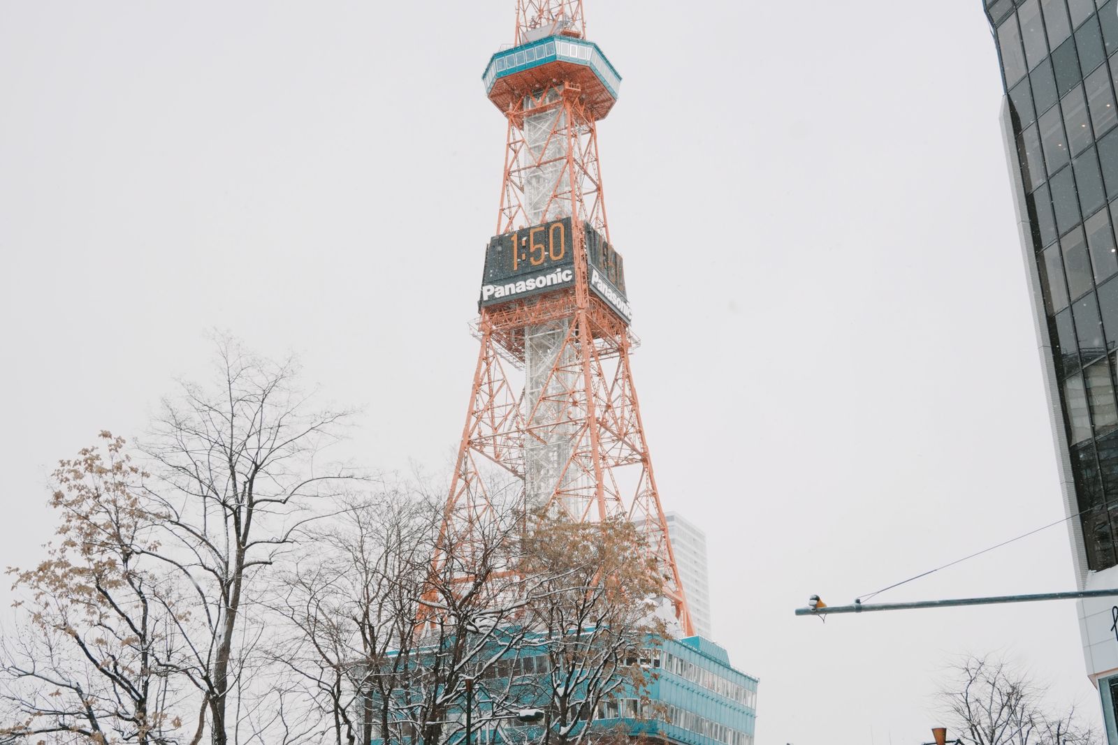 The Sapporo TV Tower on a snowy winter day, bare trees and a snow-covered street at its base.