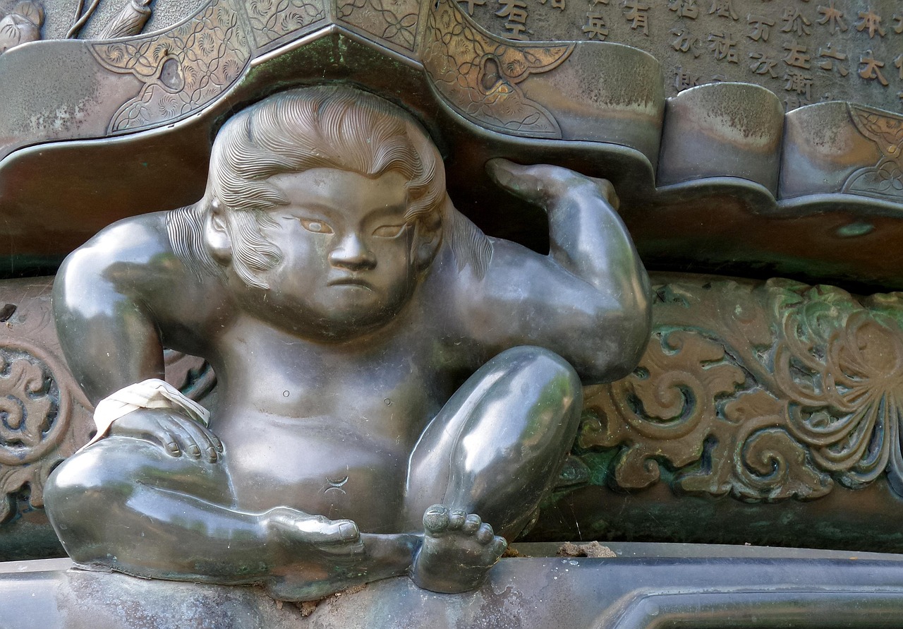 A bronze lantern held up by a carved child figure with a frown, kanji inscription behind it