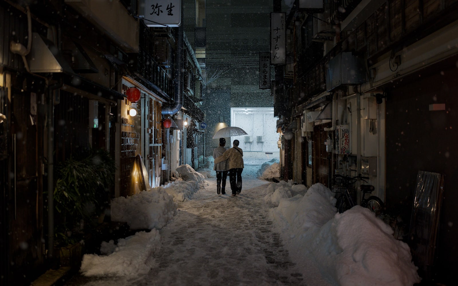 Two people under one umbrella walking down a snowy lane between old wooden houses at night, Kanazawa.