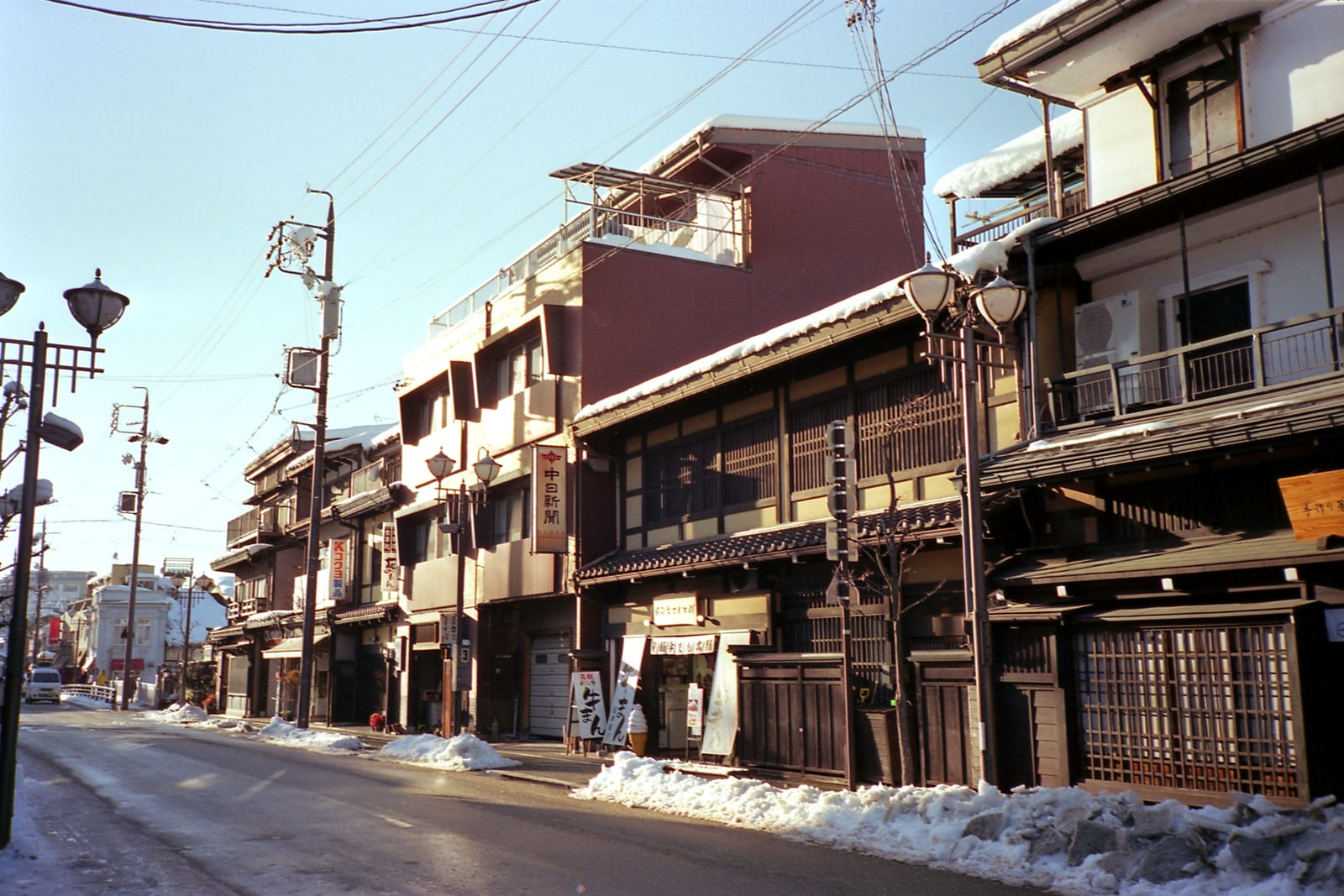 A street of old two-story wooden merchant houses with dark lattice fronts, snow along the curb, Takayama.