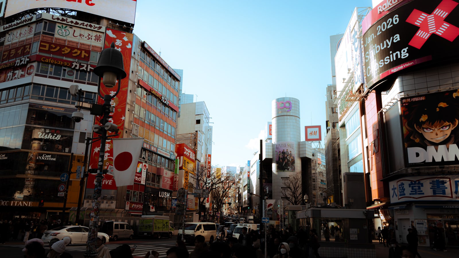 The cylindrical SHIBUYA109 tower seen from the Scramble Crossing in daylight, with large video screens and billboards on both sides