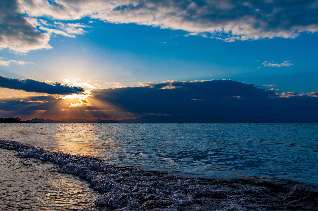 Small waves on a lake shore at sunset, sun rays fanning out through dark clouds