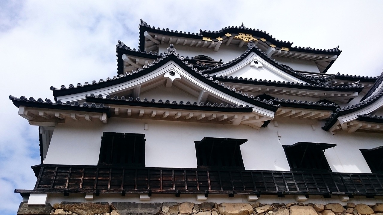 The keep of Hikone Castle seen from below: white gables with gold ornaments, black wooden boarding and a stone base