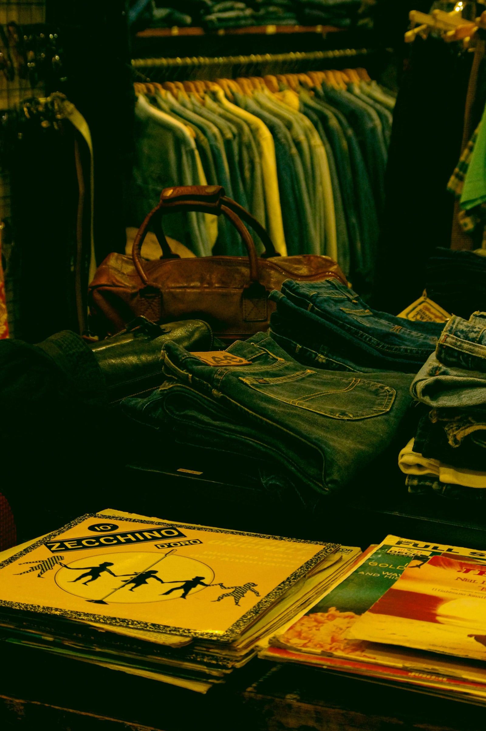 Secondhand denim shirts on a rail, folded jeans and old records in a small clothing shop