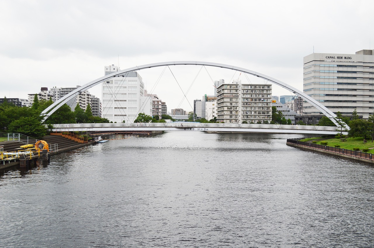 A white arch footbridge over a wide canal in Shinagawa on an overcast day, apartment and office blocks beyond