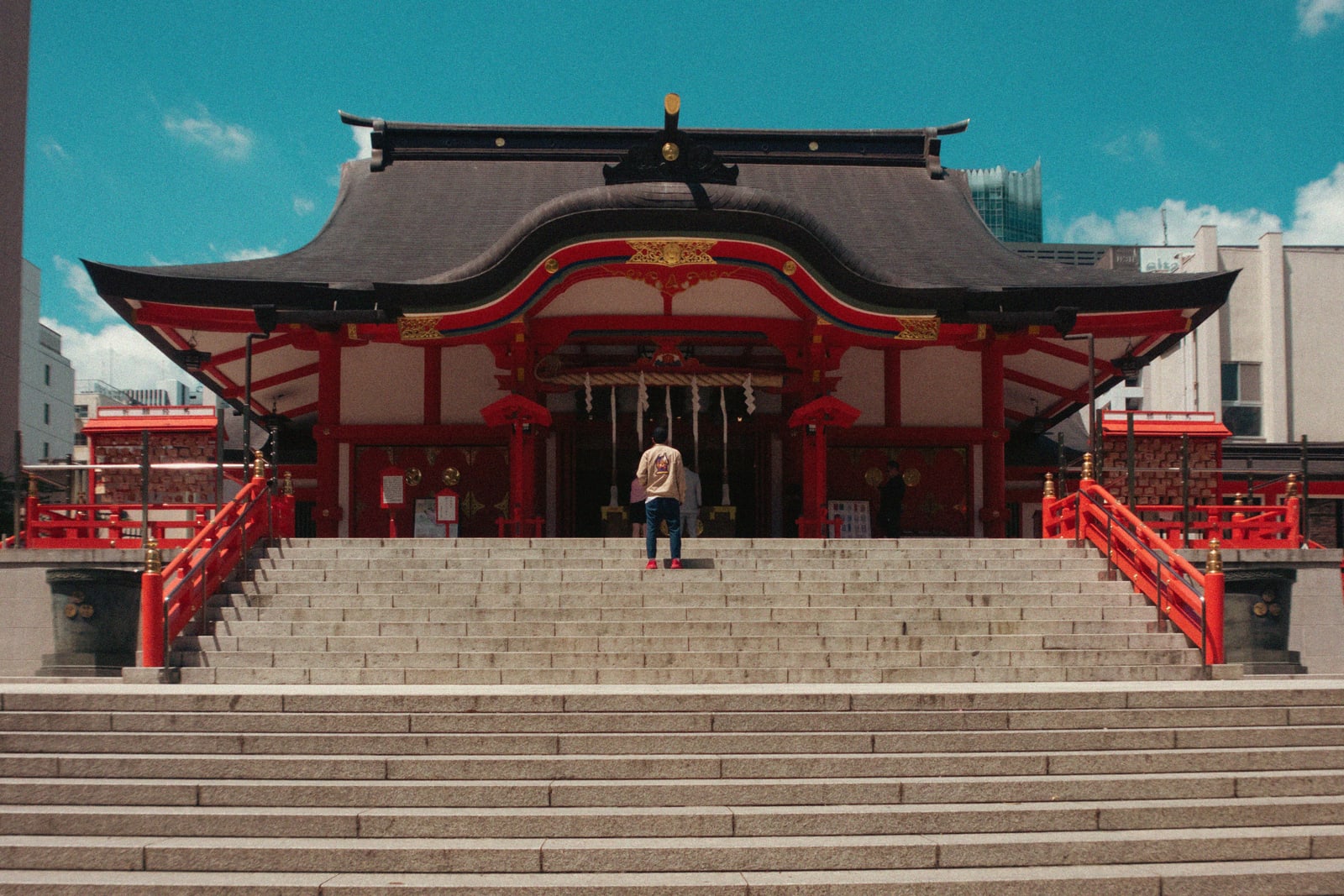 A red-and-white shrine hall with a dark curved roof behind a wide flight of stone steps