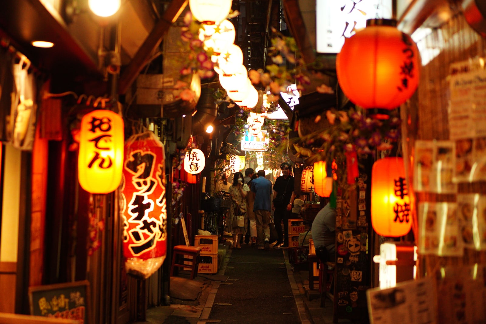 A narrow night alley under rows of red and white paper lanterns, with a few walkers far down the lane