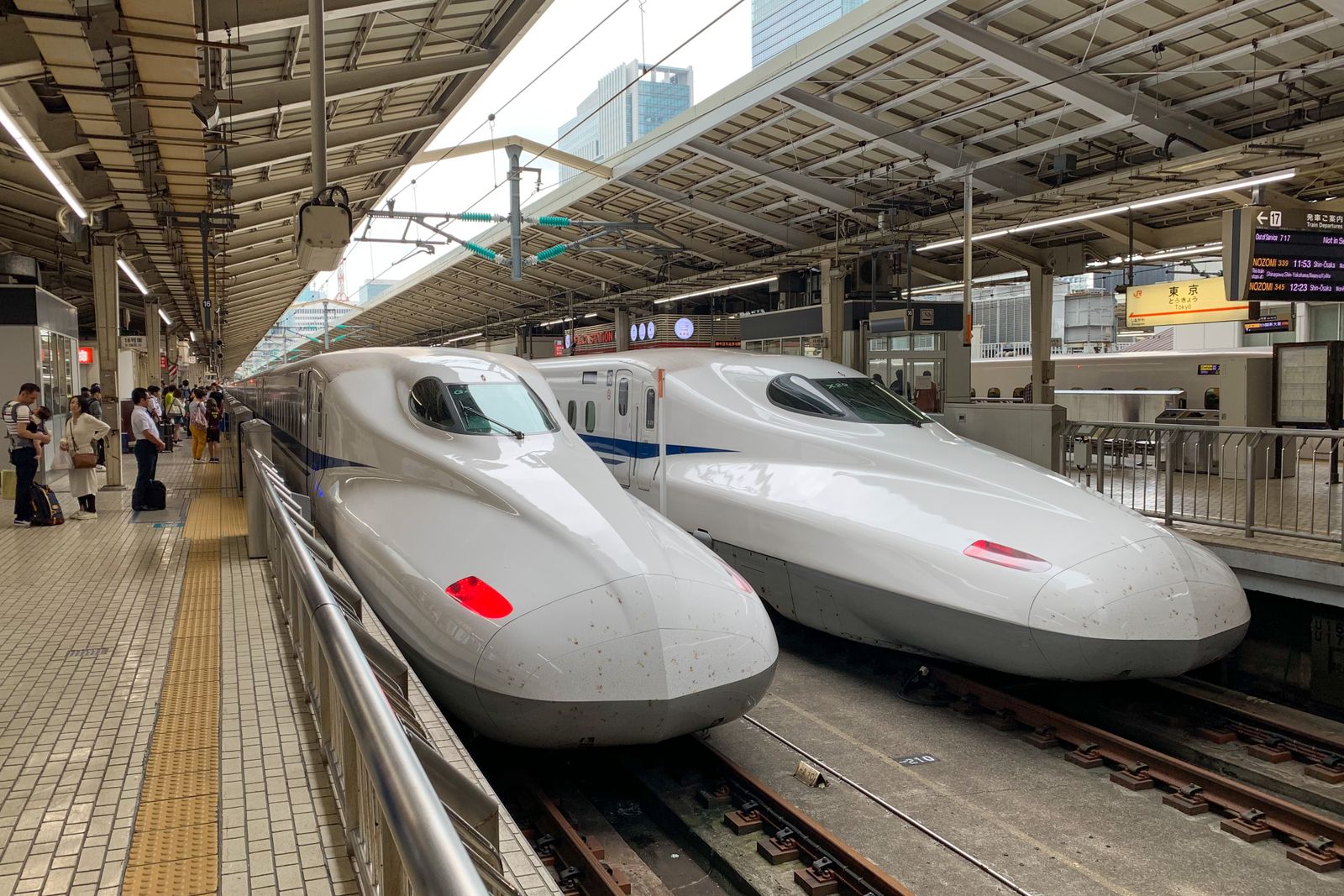 Two white Shinkansen trains side by side at a covered platform, passengers waiting along the yellow tactile line.