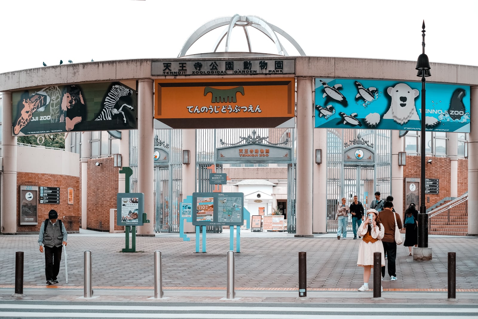 The round entrance gateway of Tennoji Zoo with animal pictures on its panels, visitors on the plaza in front