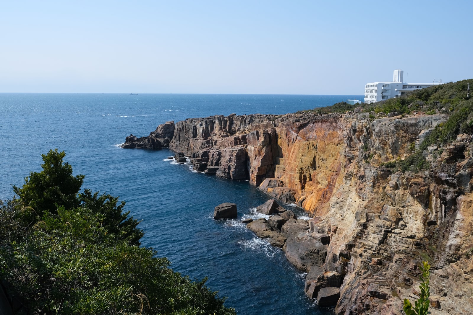 Sheer layered sea cliffs above deep blue water, a white building on the clifftop