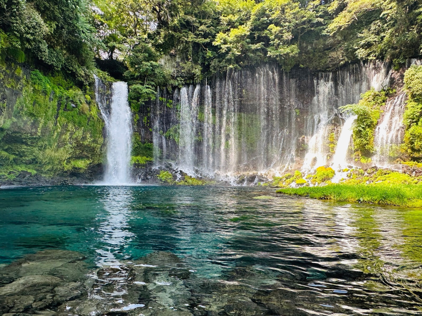 Shiraito Falls: many thin streams falling from a mossy curved cliff into a clear blue-green pool