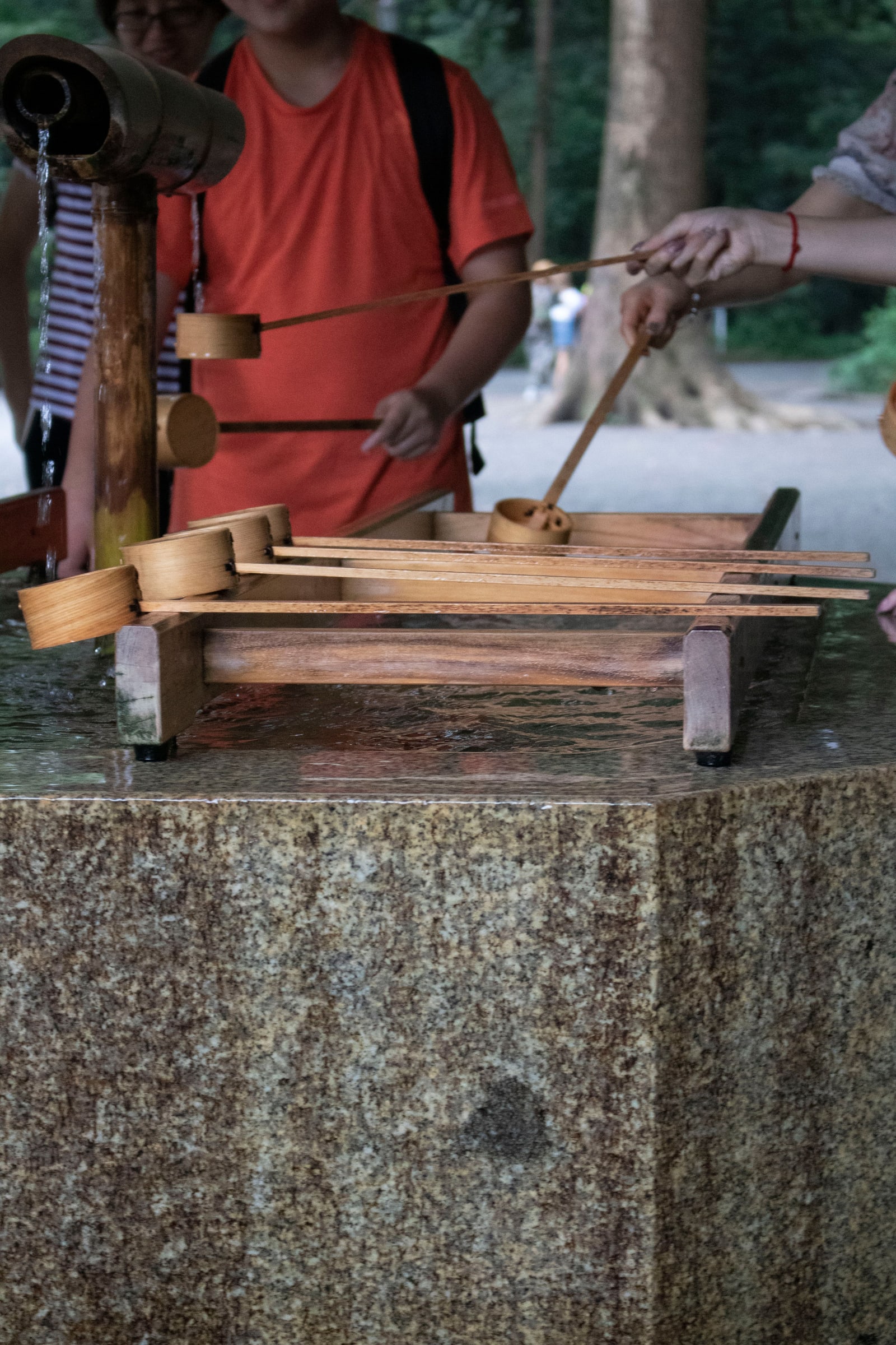 Visitors performing temizu, the hand-purification ritual, at a shrine's water basin.