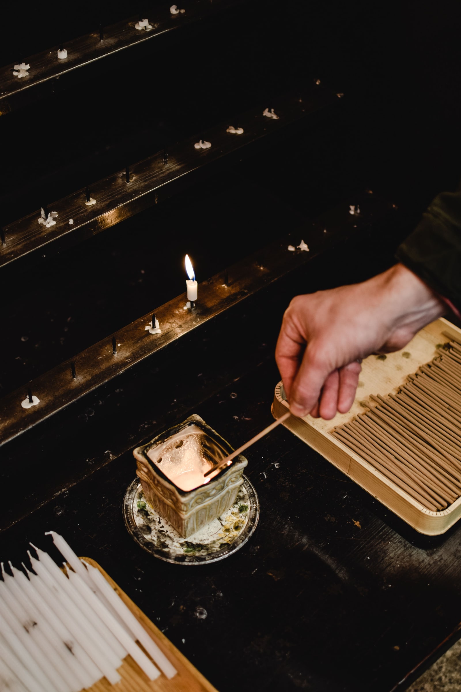 A hand lighting an incense stick at a temple's candle stand.