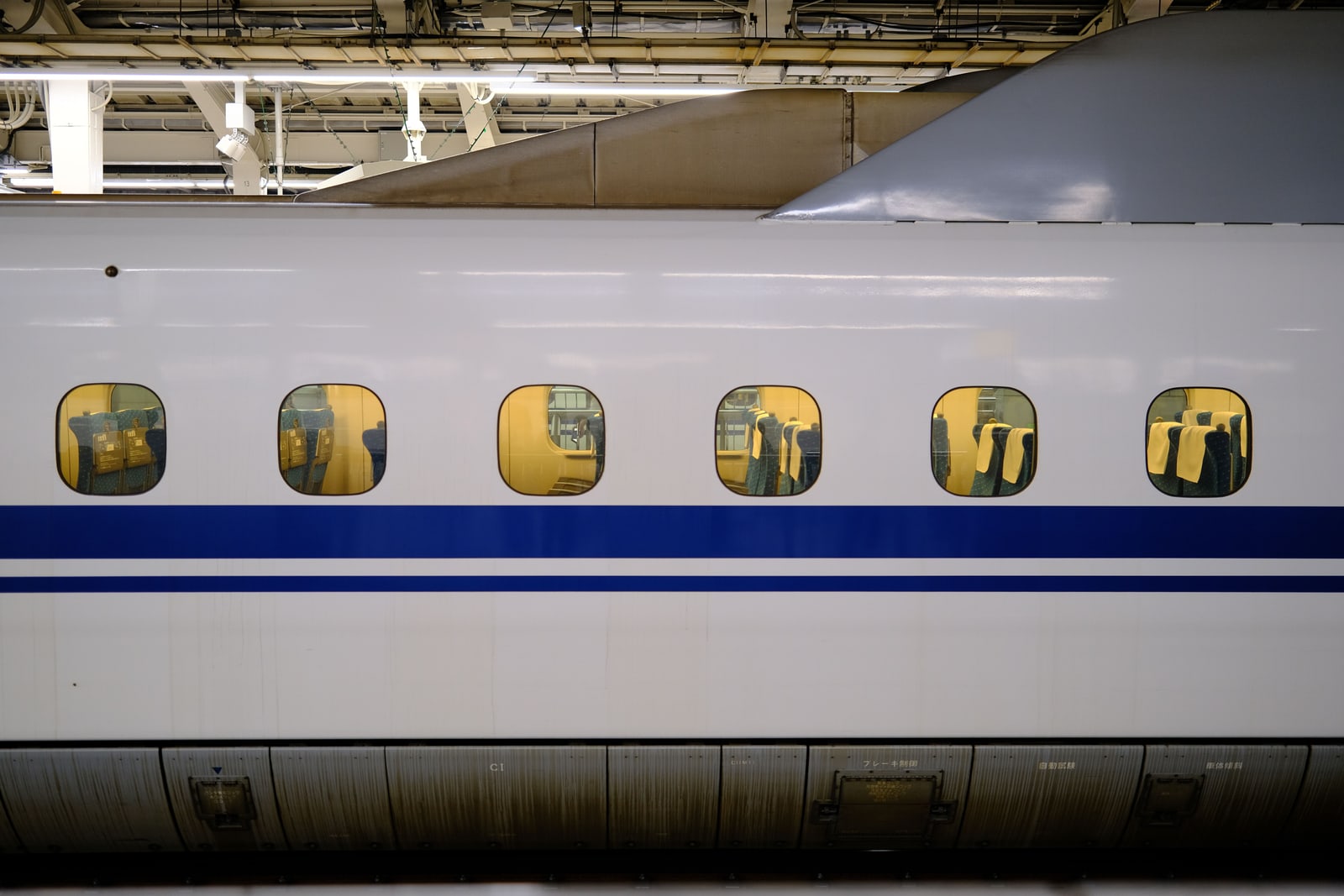 The side of a white Shinkansen train with a blue stripe, stopped under the roof of a Tokyo Station platform.