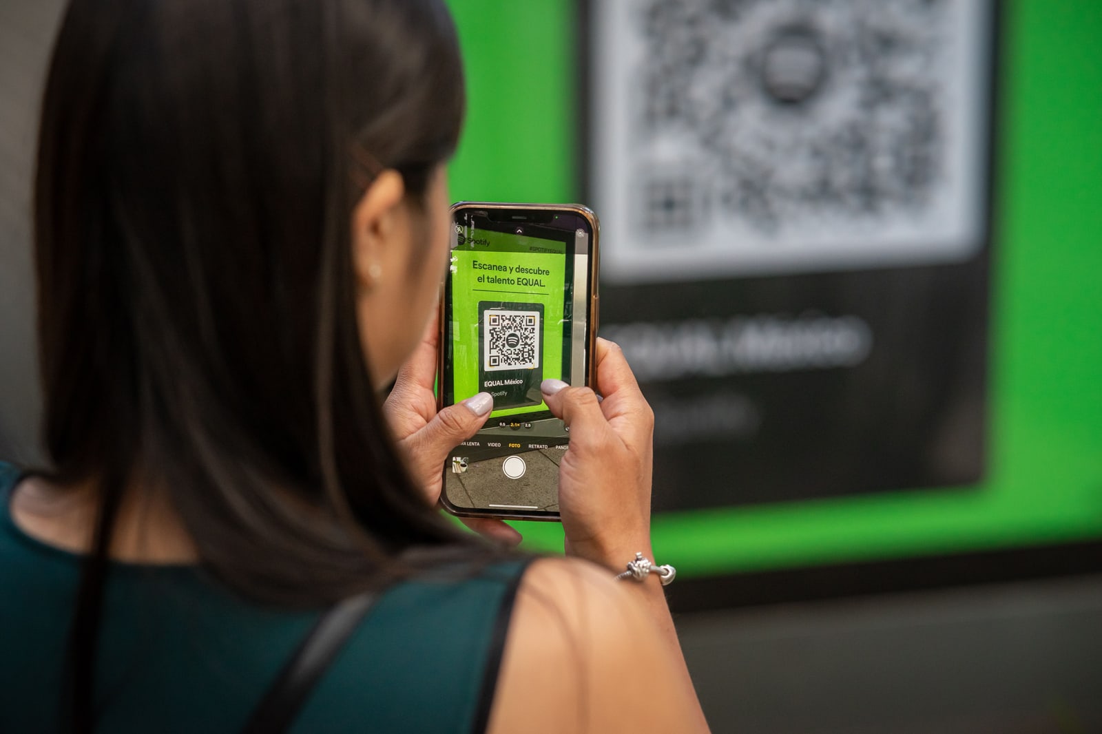 A woman seen from behind holding up a smartphone that shows a QR code.