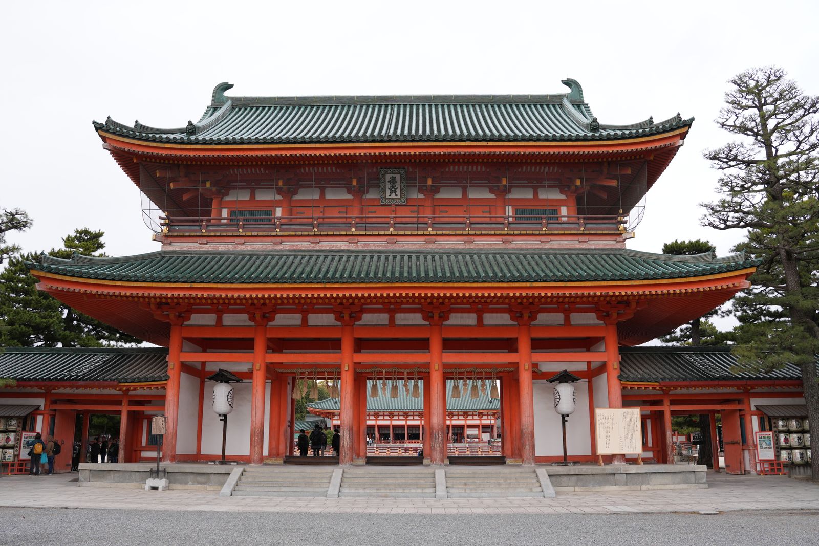 The two-story vermilion Otenmon gate of Heian Shrine with green-tiled roofs, a few distant visitors under the gate.