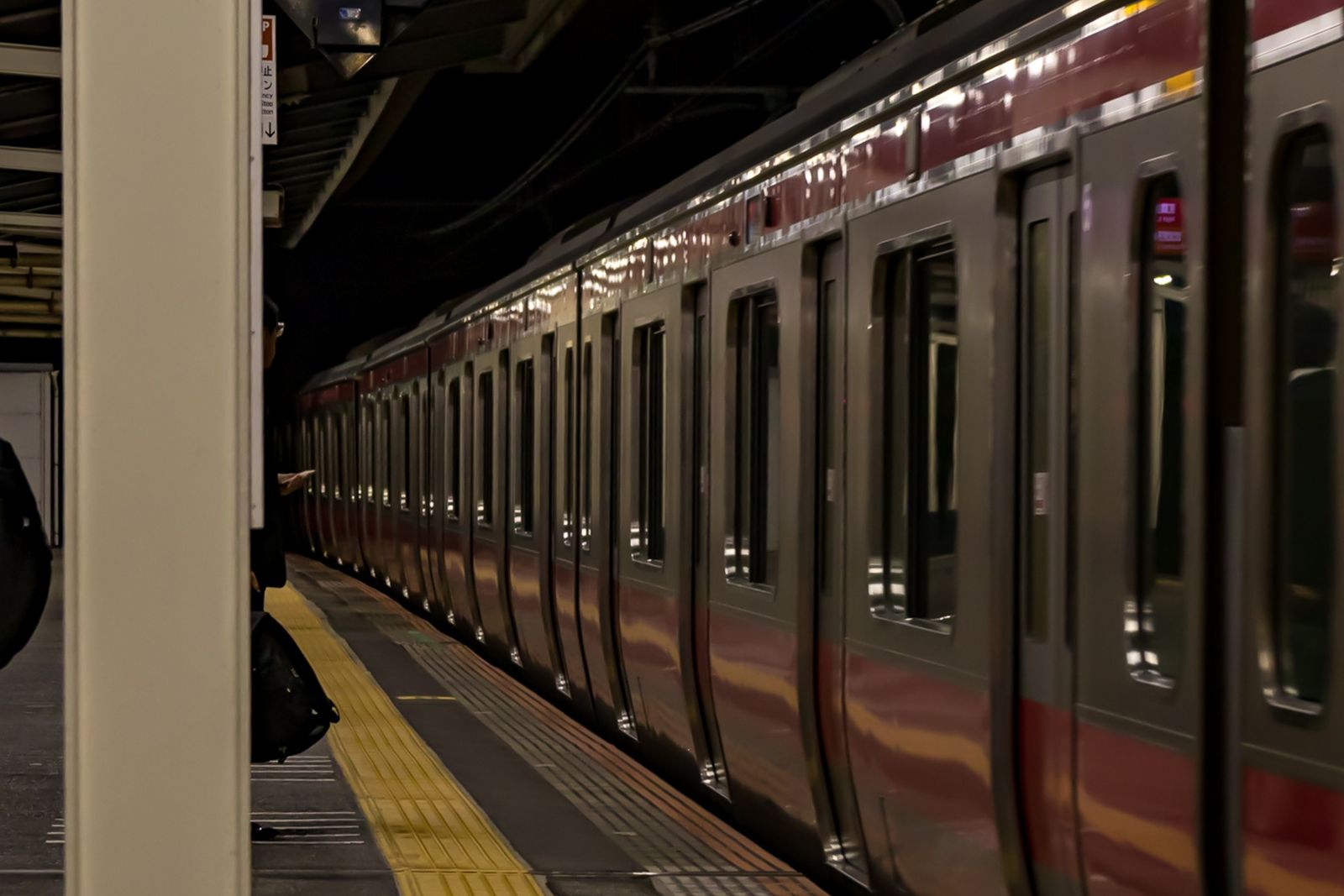 A dark, near-empty Tokyo platform at night with a single waiting passenger.