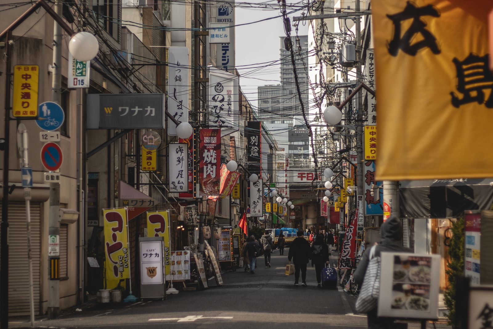A covered shopping street in Namba, Osaka, with a 千日前 中央通り sign overhead.