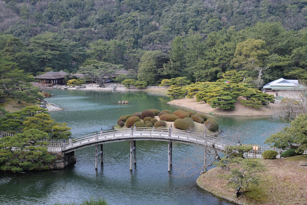An arched wooden bridge over a pond in Ritsurin Garden, a teahouse on the far shore and a wooded hill behind