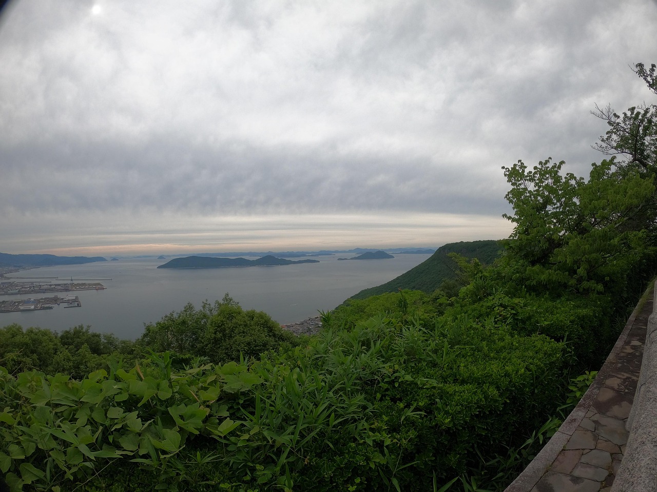 A view from a high wooded ridge over a calm sea and low islands under grey cloud
