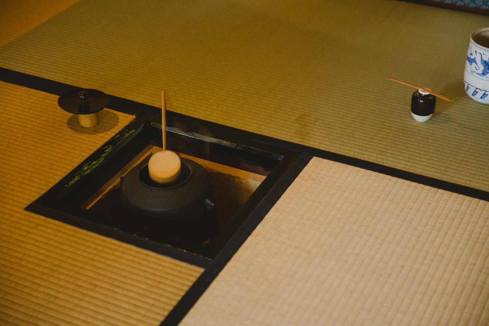 A sunken hearth with an iron kettle, a bamboo whisk on its stand and an incense box on tatami.