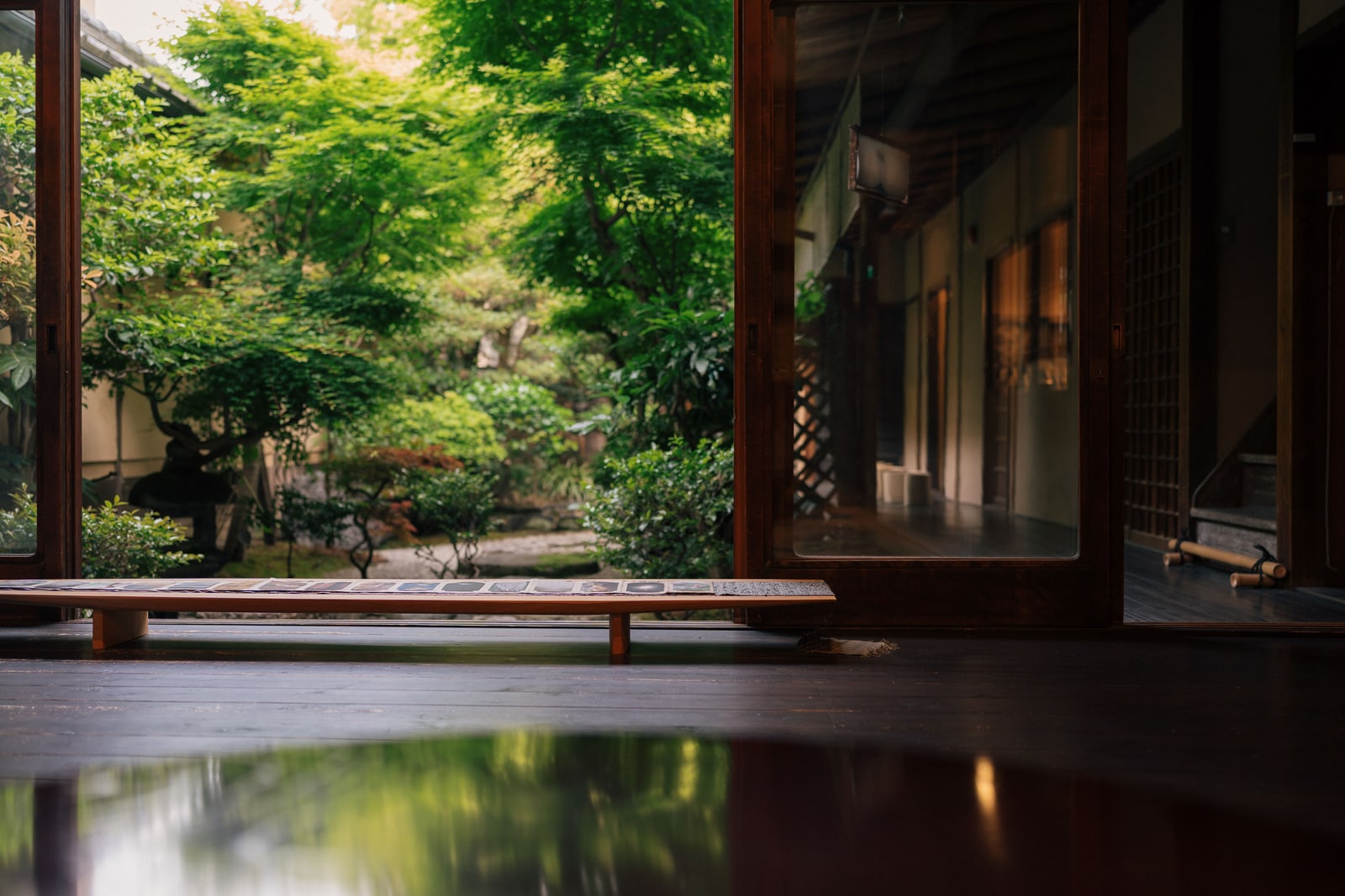 A view from a wooden veranda through open sliding doors onto a green garden, in Kyoto.