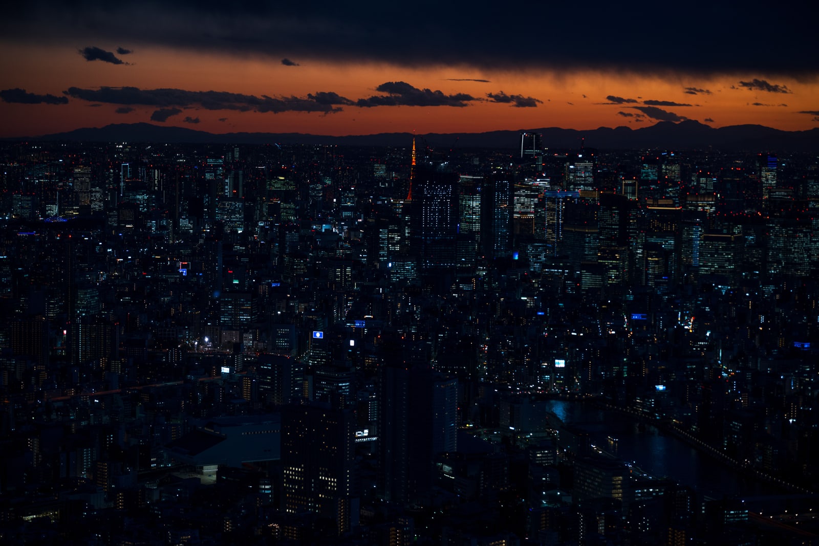 Tokyo seen from above at dusk, city lights under an orange sky.