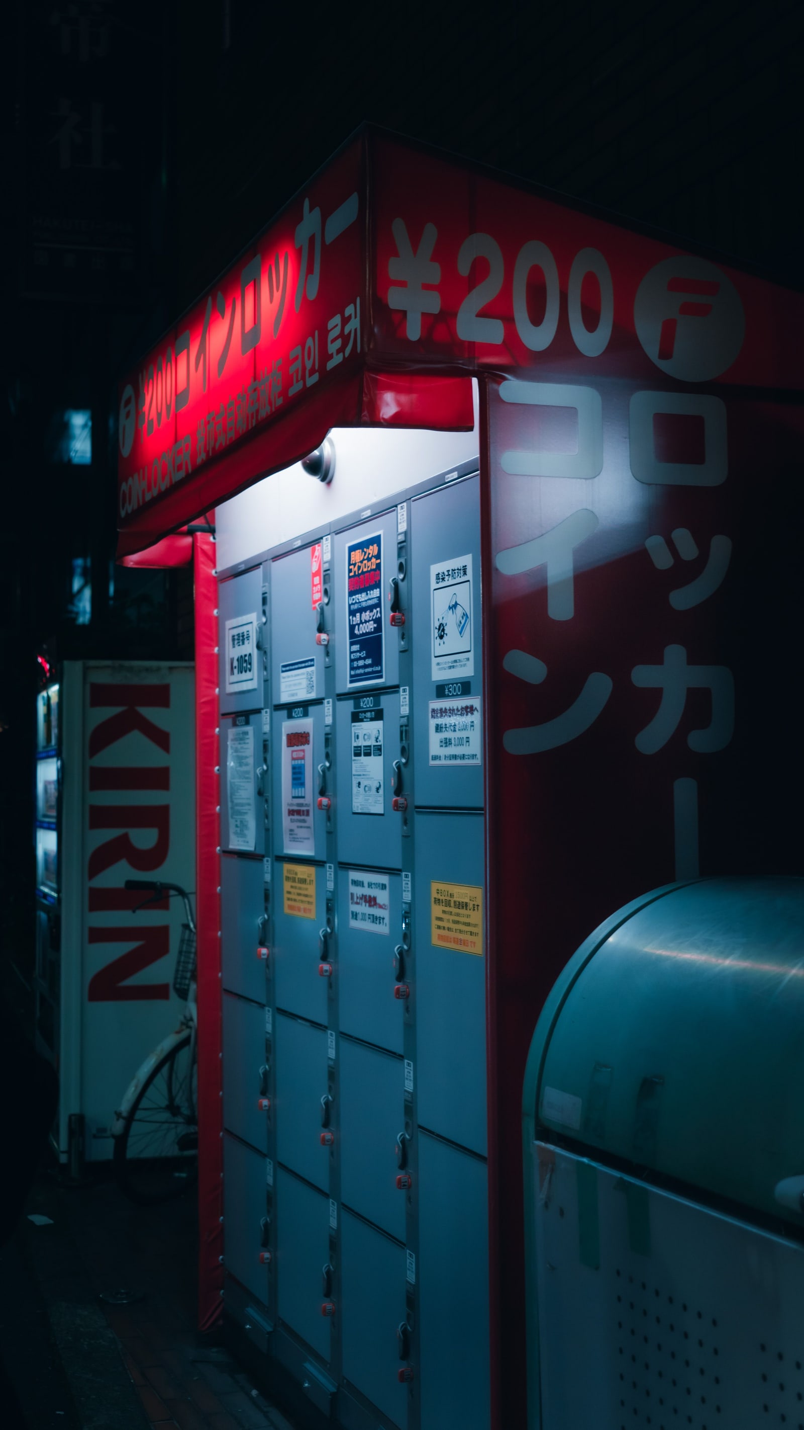 A row of coin lockers under a red sign on a street at night.