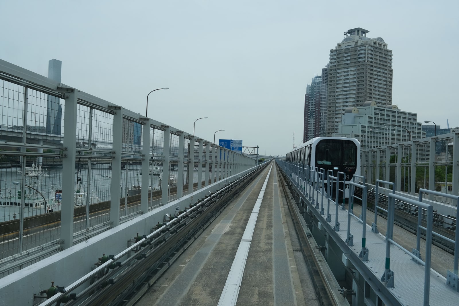 A driverless train on an elevated guideway beside the water, with high-rise buildings behind.