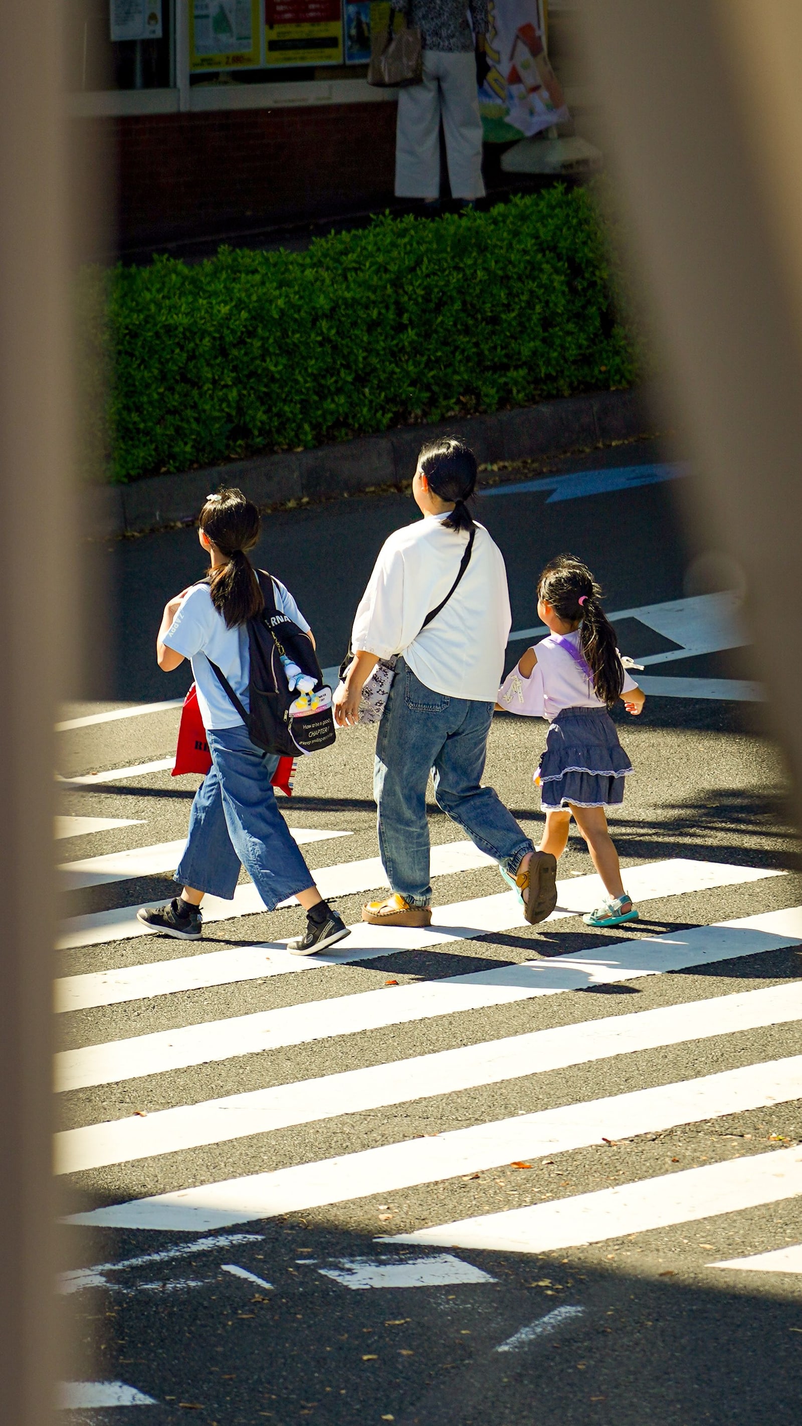 An adult and two children crossing a street hand in hand in Tokyo.