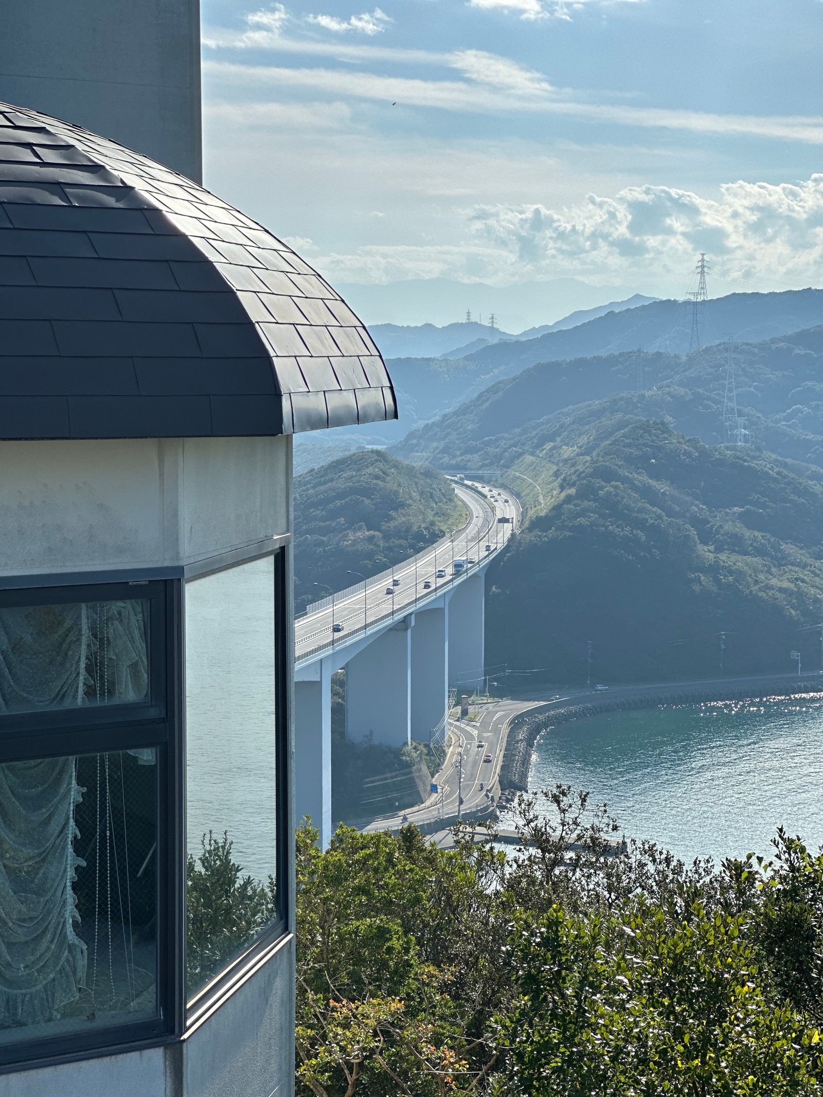 An elevated expressway curving between wooded hills above a coastal road