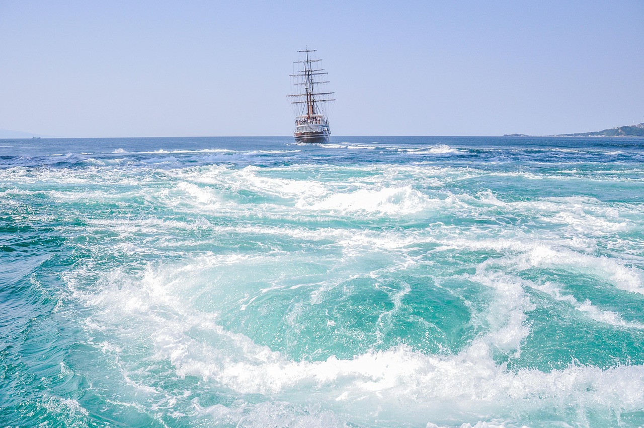 Swirling turquoise sea water with a tall-masted sightseeing boat in the distance