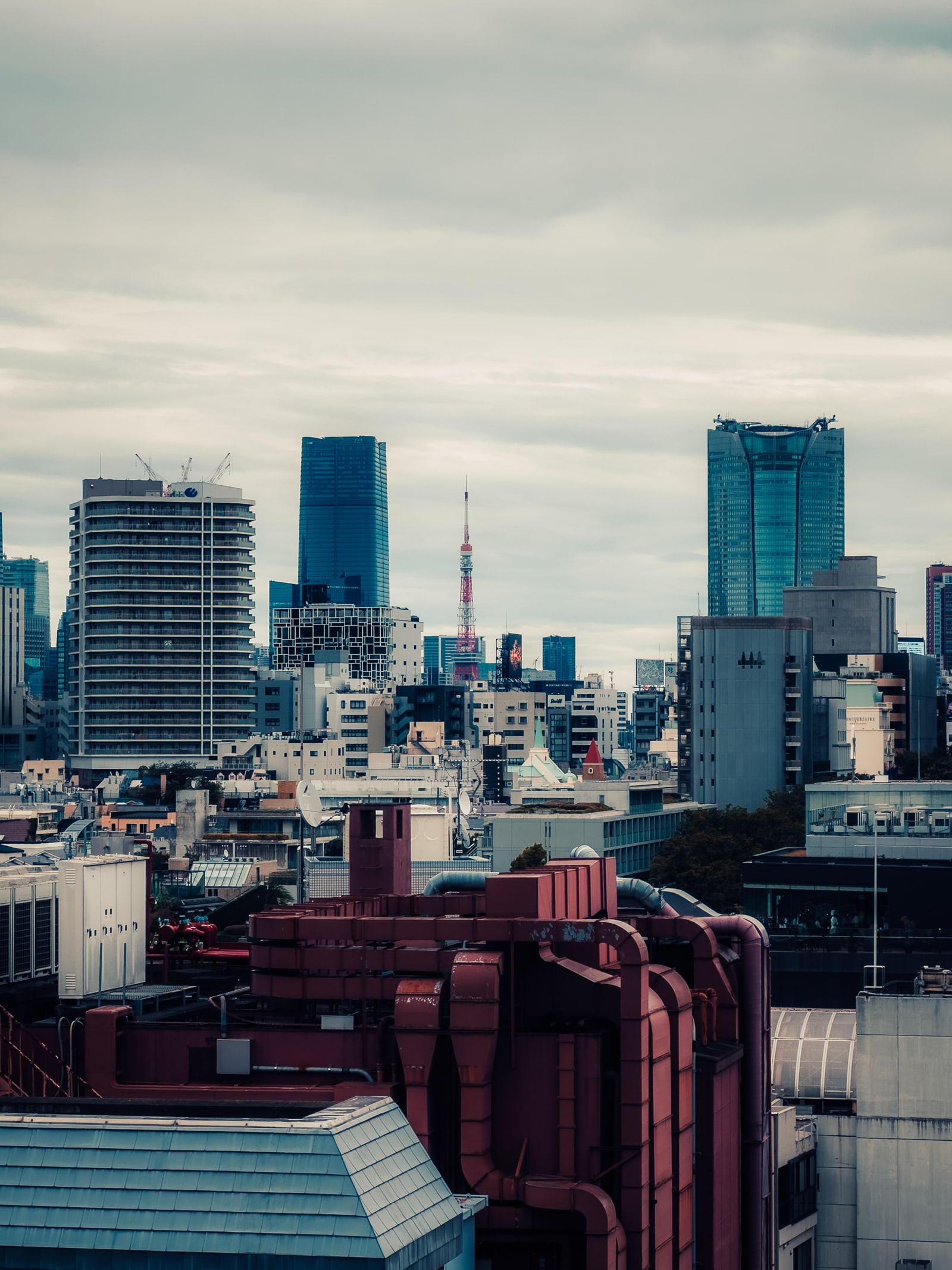 Tokyo Tower and the Minato skyline under a flat overcast sky, seen over rooftops.
