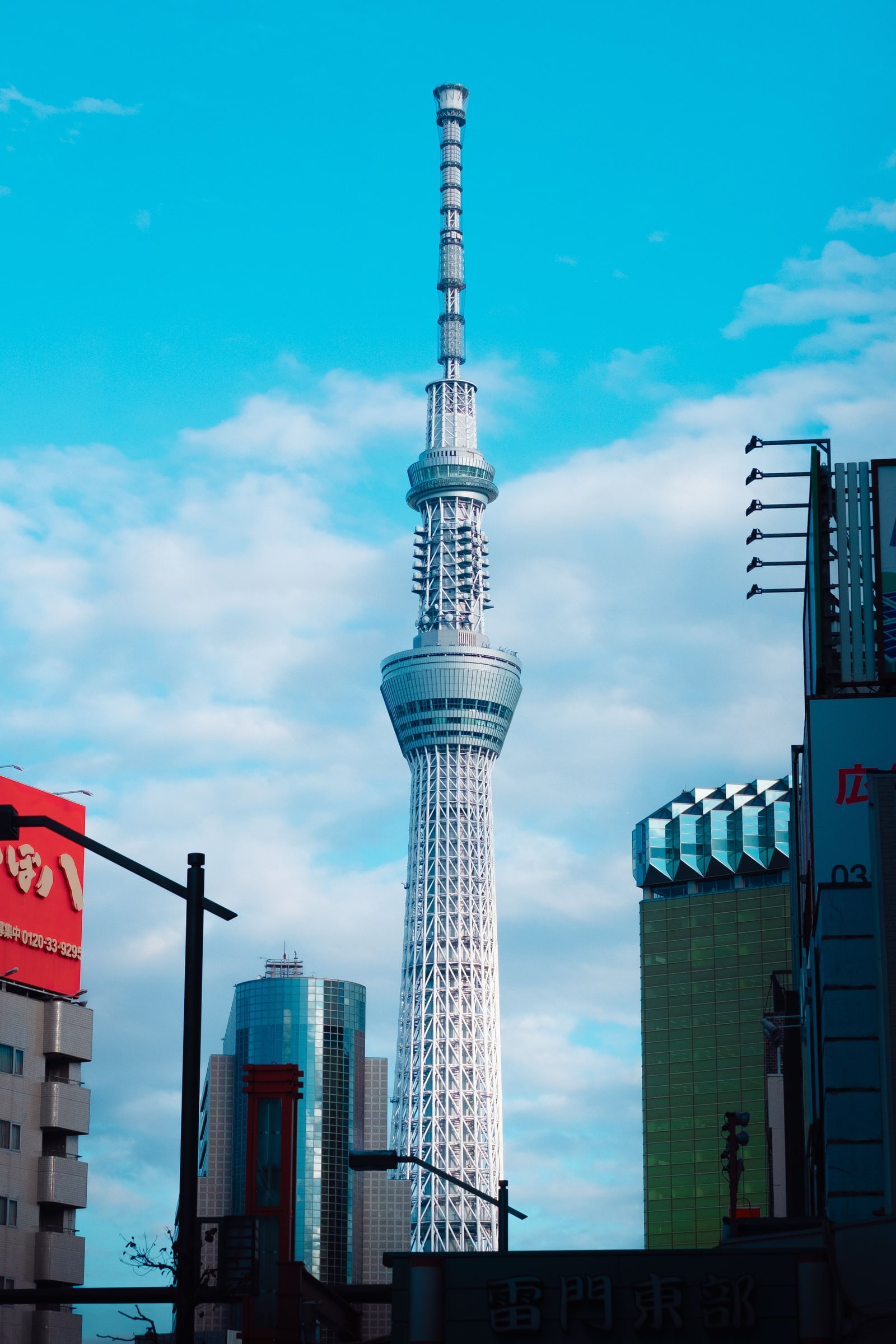 Tokyo Skytree seen from street level under a blue sky, low buildings and signboards in the foreground.